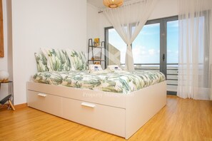 A bedroom with a bed, a nightstand, a bookshelf, and a view of the sea through a balcony. - Casa Menezes (Casal do Labrusque)