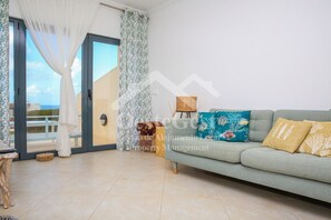 A living room with a grey sofa, a patterned cushion, and a view through a glass door.