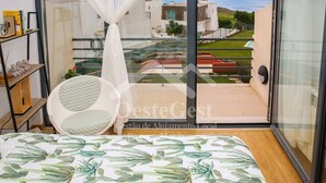 Ein Schlafzimmer mit Bett, Stuhl, Bücherregal und Blick ins Freie.