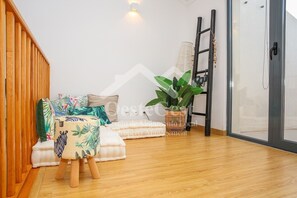 A modern living room with a wooden floor, a sofa with patterned cushions, a small wooden stool, a potted plant, and a ladder against the wall. - Casa Menezes (Casal do Labrusque)