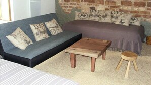 A cozy room with a brick wall, a grey sofa with 'LOVE' pillows, a small wooden table, and a stool.