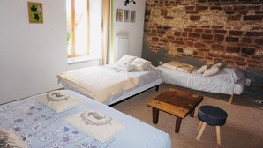 A bedroom with two beds, a wooden table, a bench, and a stone wall.