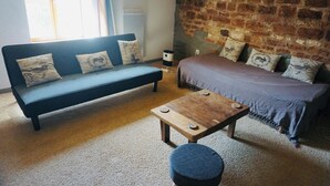 A cozy room with a blue sofa, a wooden table, and a bed with patterned pillows.