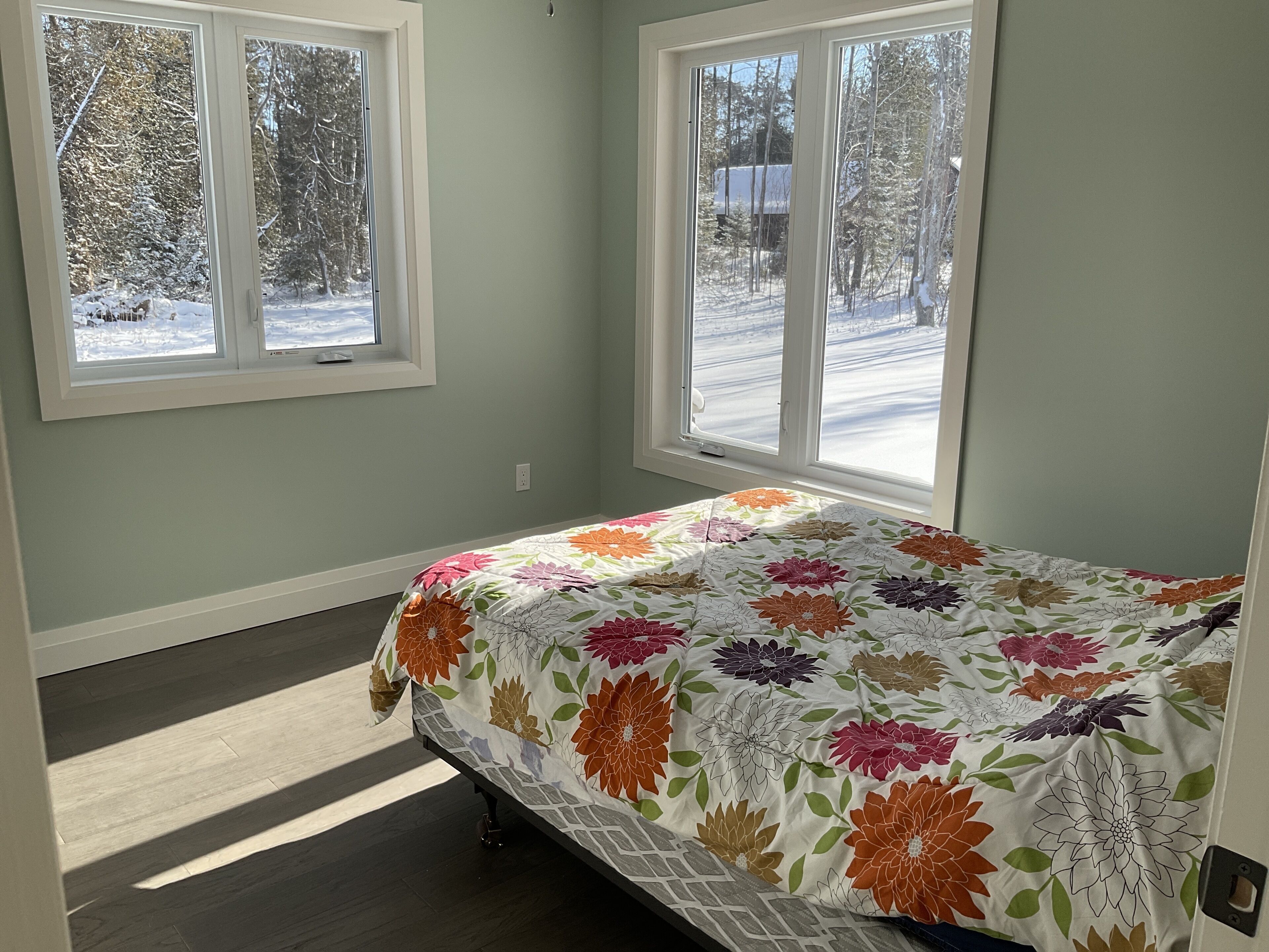 A bedroom with a bed, two windows, and a view of a snowy landscape.