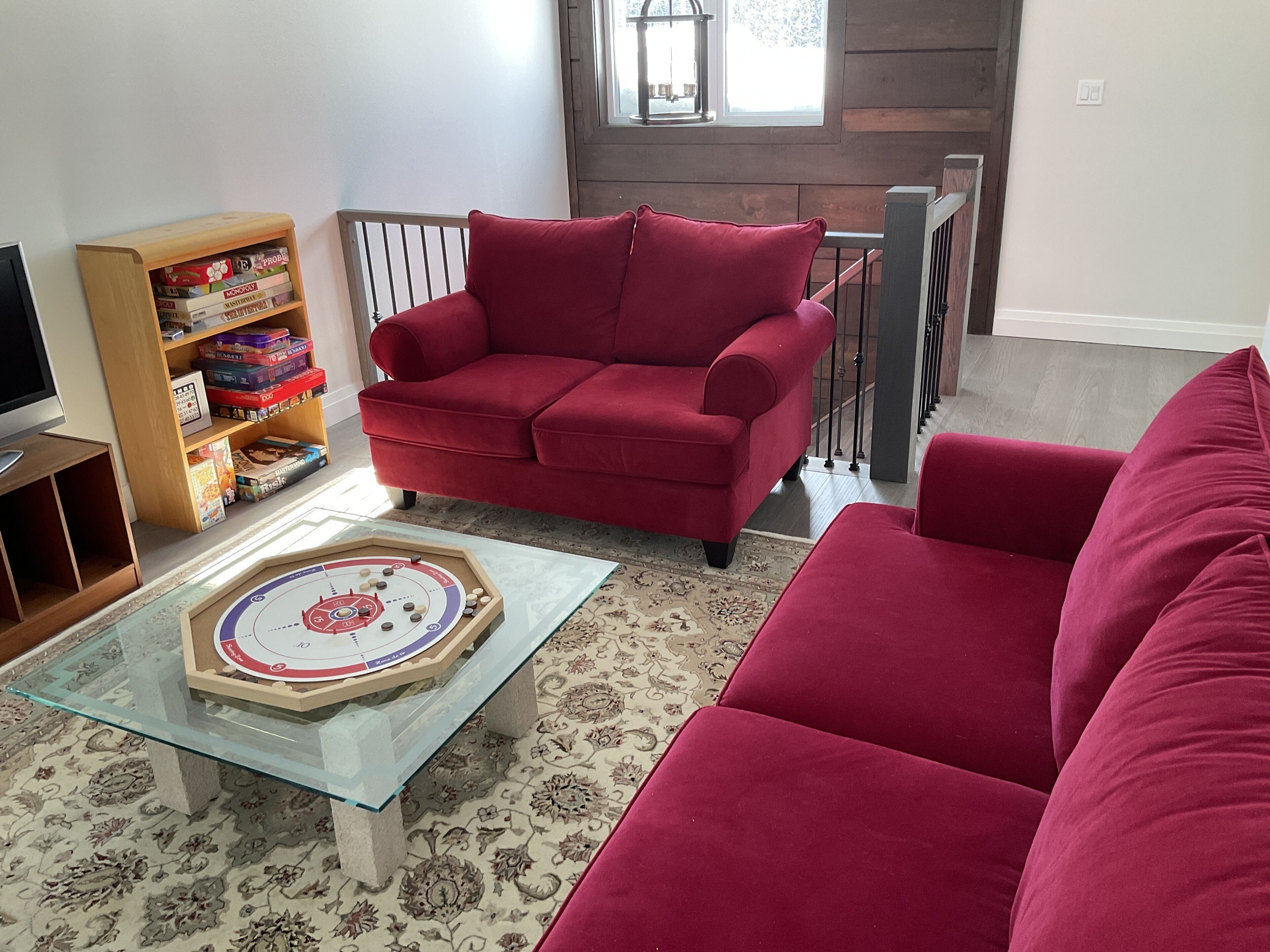 Un salon avec un canapé rouge, une table basse en verre et une bibliothèque remplie de jeux de société.