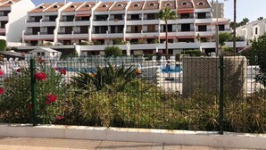 A hotel with multiple balconies, a swimming pool, and a fenced garden area.