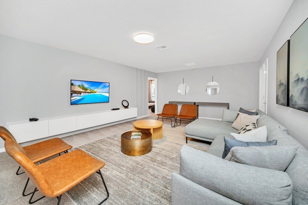 A modern living room with a flat-screen TV, a sofa, two armchairs, a coffee table, and a sideboard.