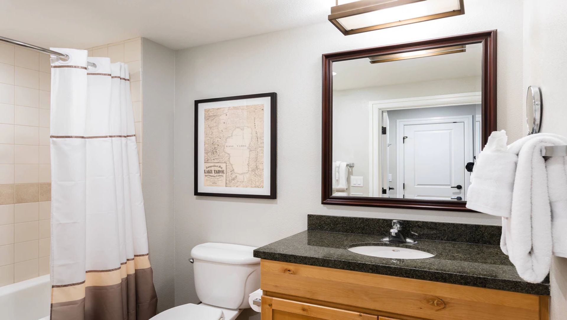 Une salle de bain avec un rideau de douche, une carte encadrée, un lavabo avec un miroir et des toilettes.