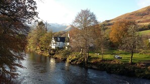 Ein weißes Haus mit schwarzem Dach, umgeben von Bäumen und einem Fluss.