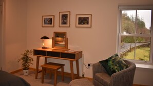 Ein Zimmer mit einem Holztisch, einem Stuhl, einer Lampe, einem Spiegel und drei gerahmten Bildern an der Wand.