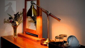 Ein Holztisch mit einer Schreibtischlampe, einem gerahmten Bild, einer Vase mit Blumen und einer Geschirrservierplatte.