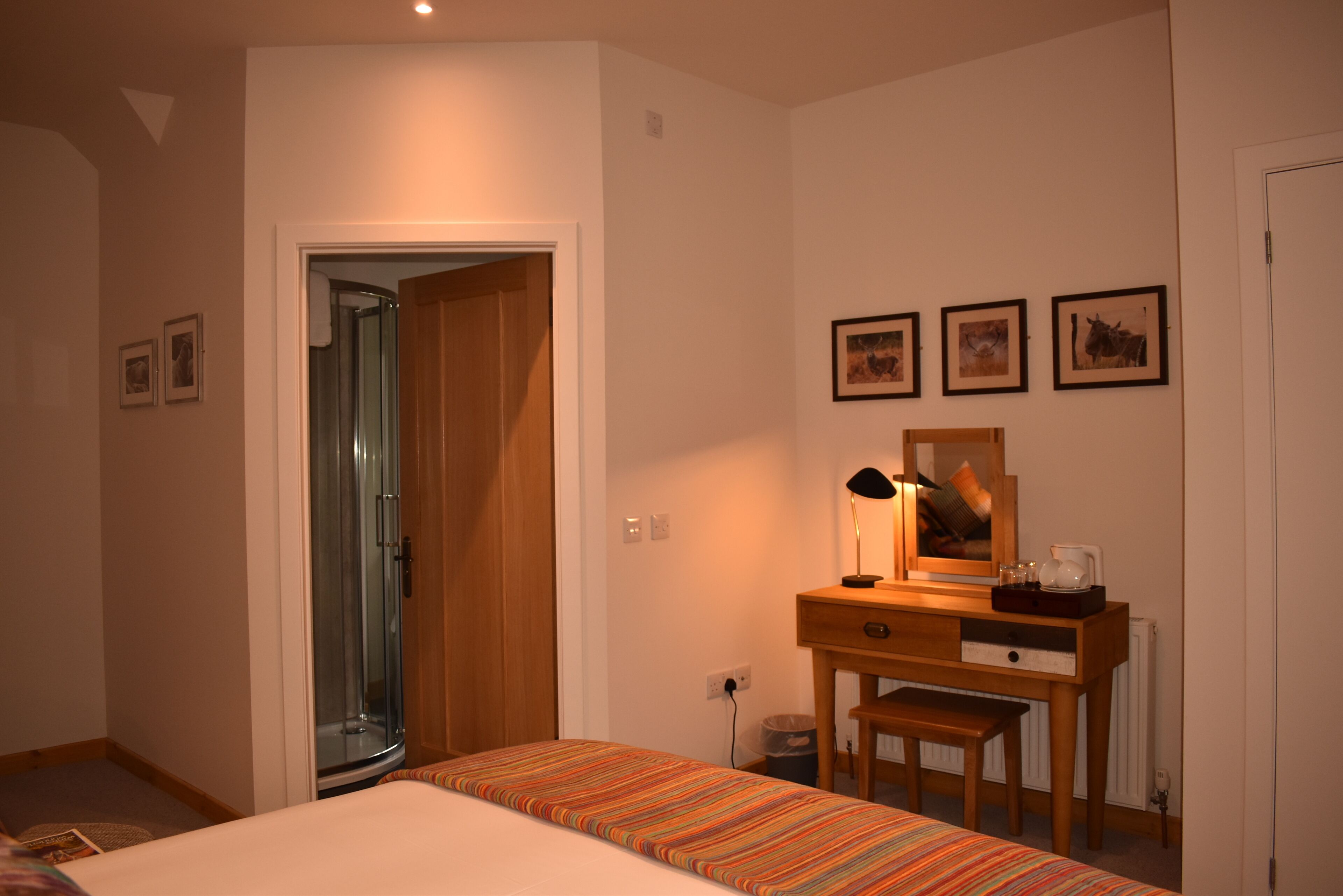 A bedroom with a bed, a wooden desk, a chair, a mirror, and framed pictures on the wall.