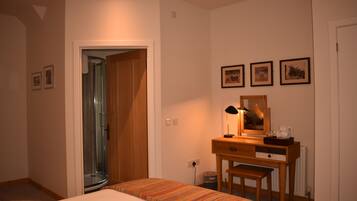 A bedroom with a bed, a wooden desk, a chair, a mirror, and framed pictures on the wall.