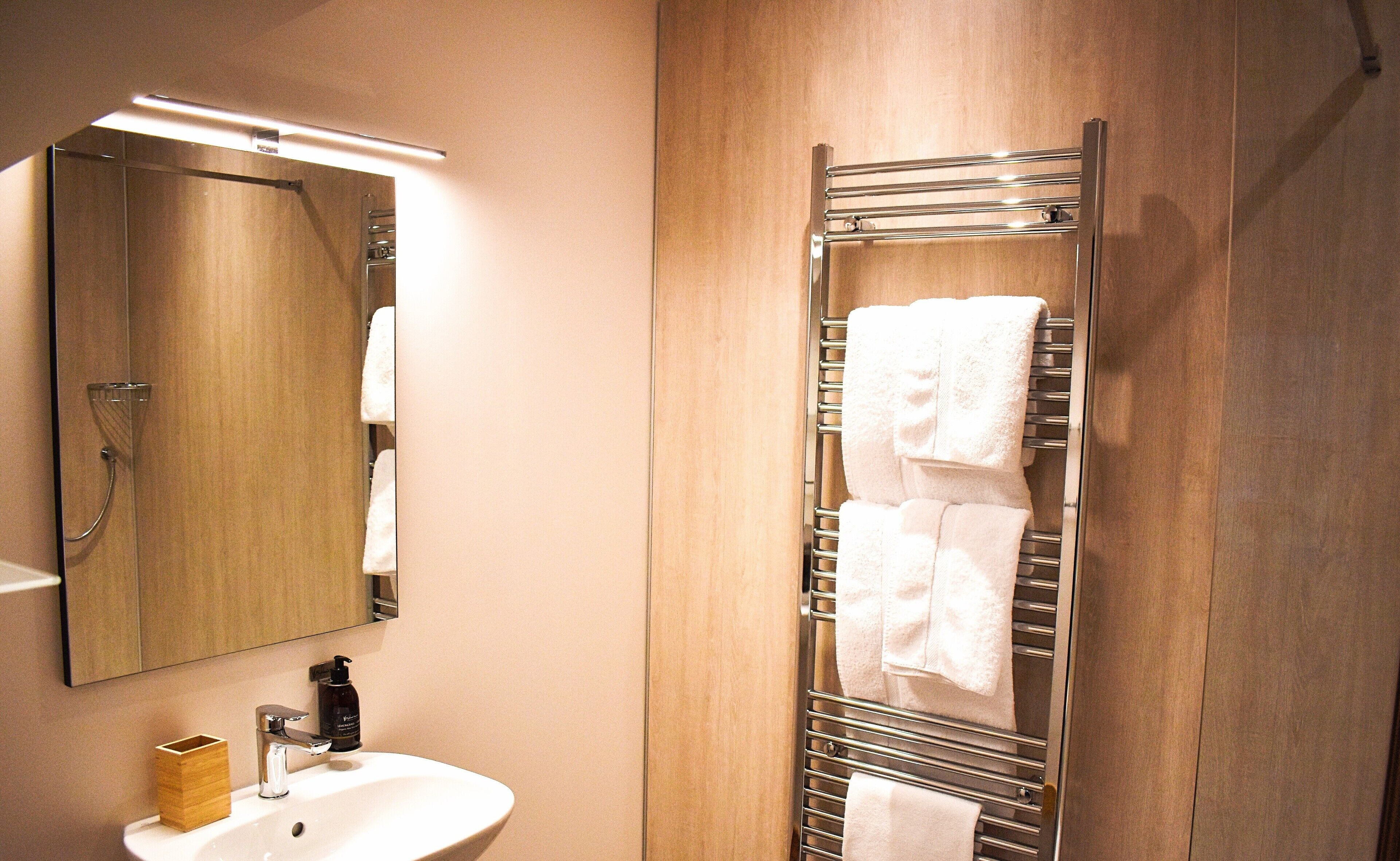 Ein Badezimmer mit einem Holzwaschtisch, einem Waschbecken, einem Spiegel und einem Handtuchhalter mit mehreren Handtüchern.
