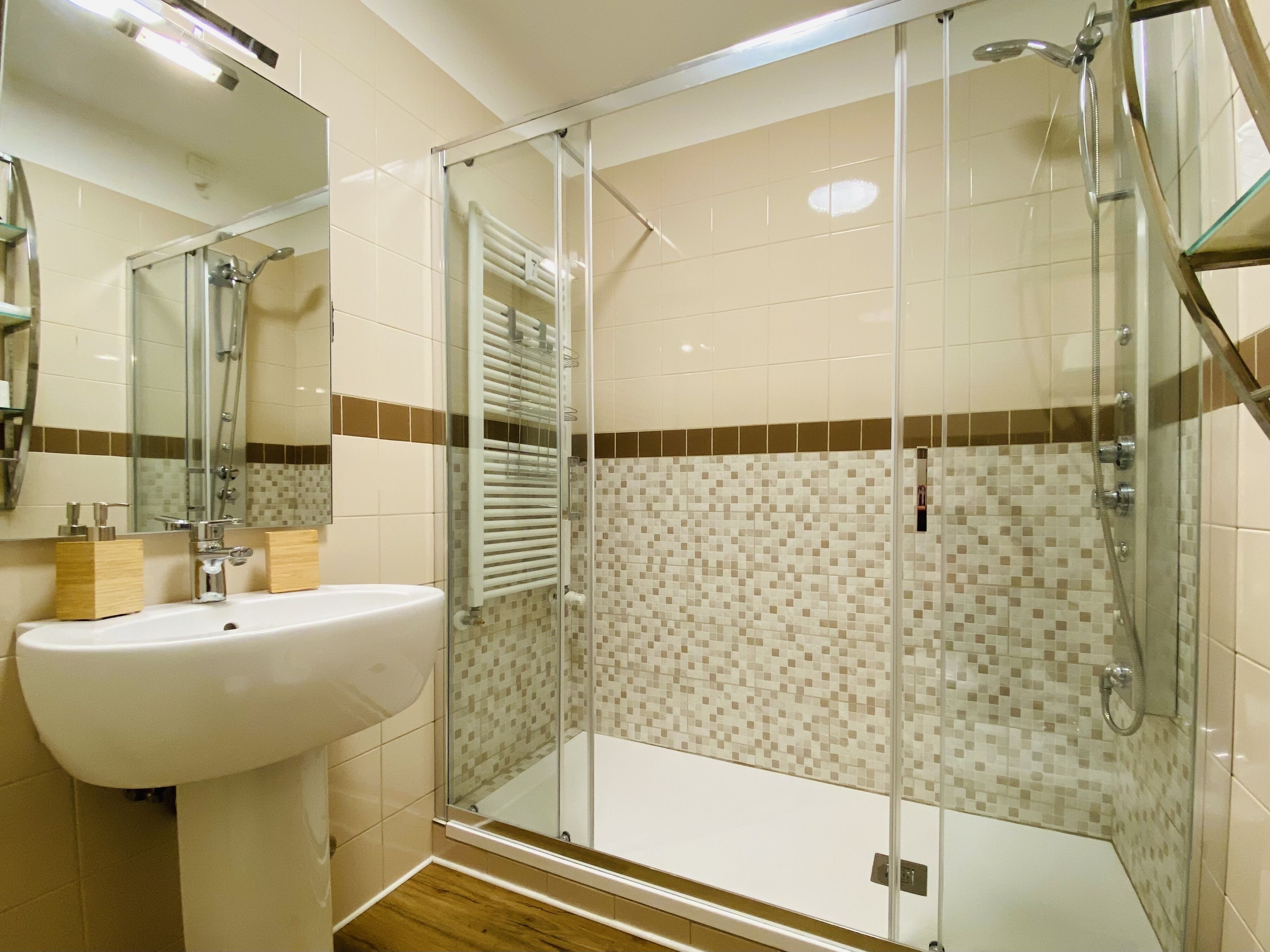 Un bagno con cabina doccia in vetro, un lavandino bianco e schienale piastrellato.