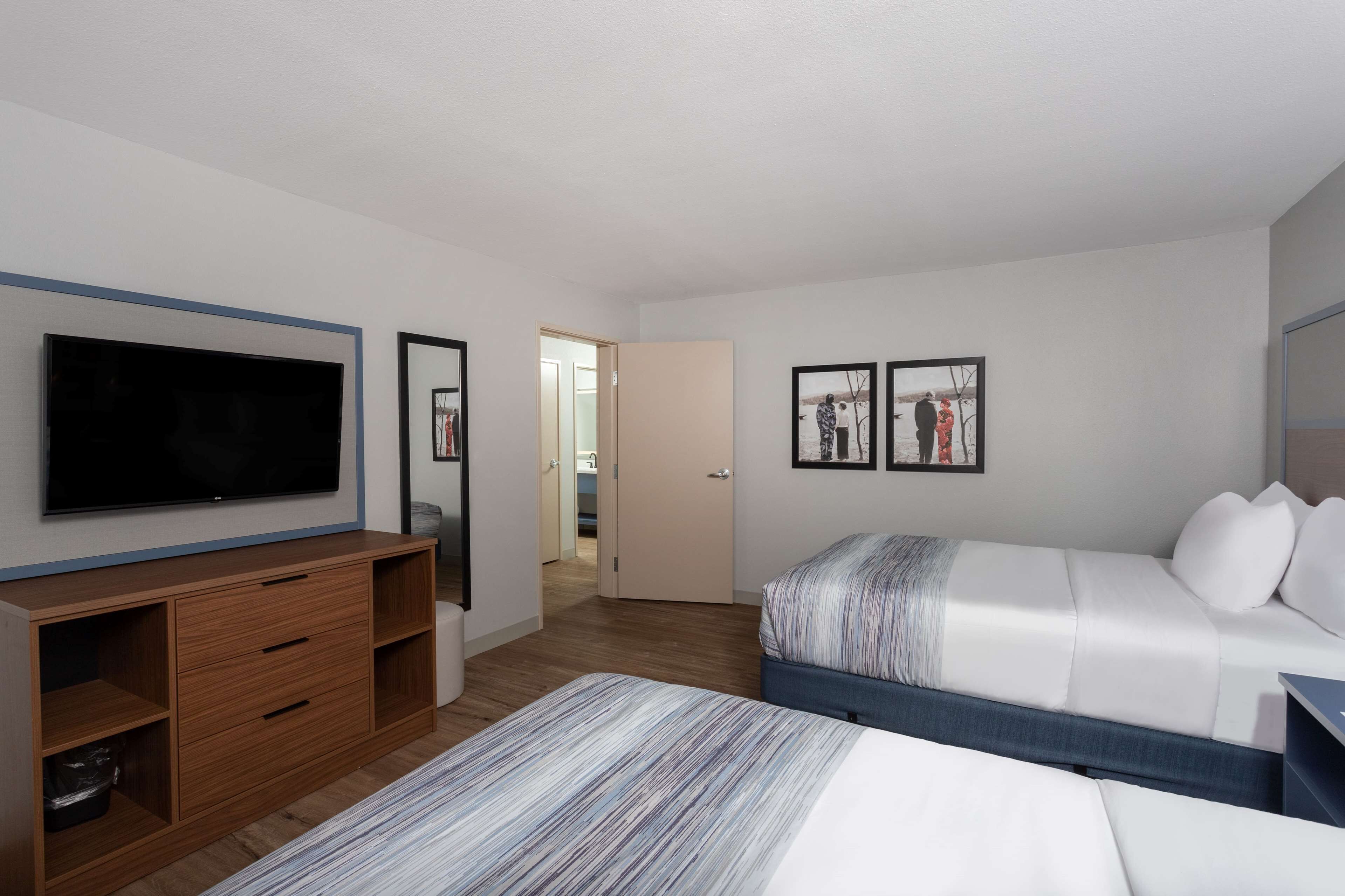 Une chambre d’hôtel moderne dotée d’un grand téléviseur à écran plat, d’une commode en bois, d’un lit recouvert d’une couverture à rayures et de deux tableaux encadrés accrochés au mur.