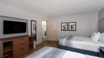 A modern hotel room with a large flat-screen TV, a wooden dresser, a bed with a striped blanket, and two framed pictures on the wall.