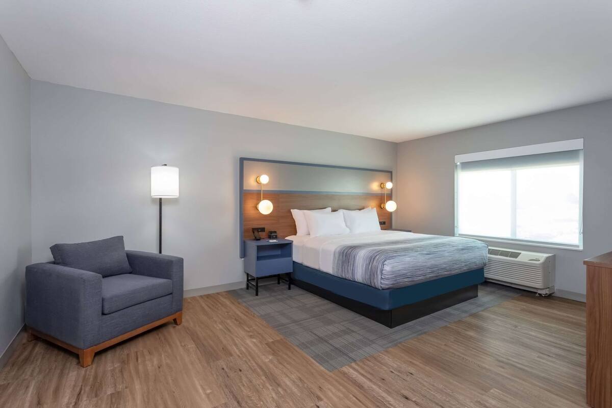 A modern hotel room with a bed, bedside table, lamp, and a chair.
