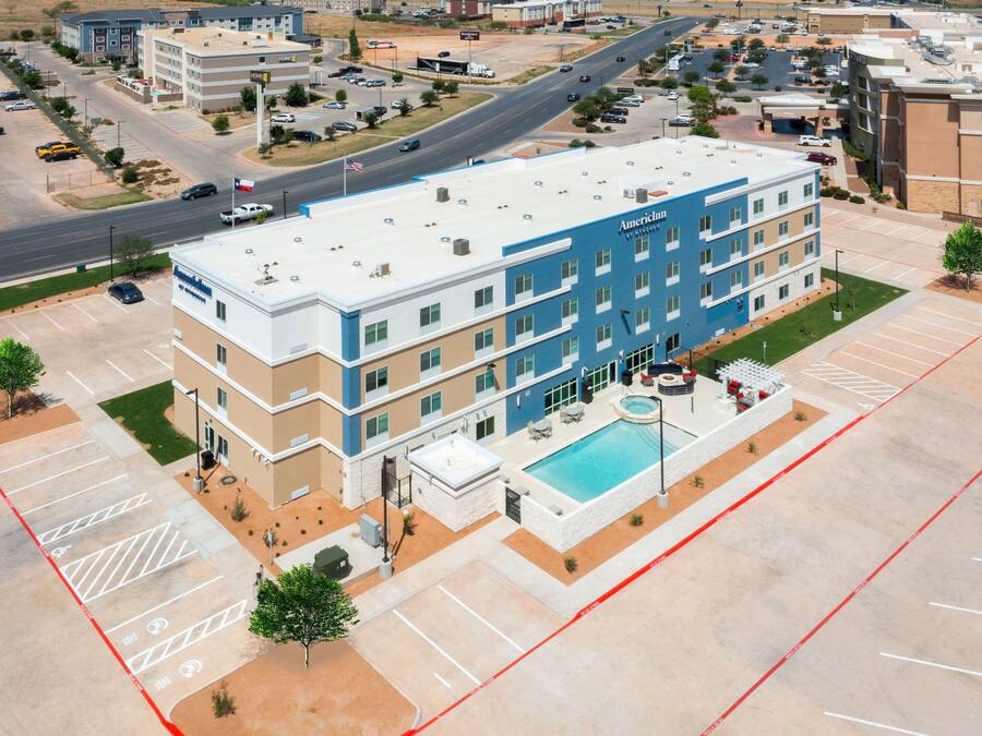 Um hotel com vários andares, piscina, estacionamento e uma estrada ao fundo.