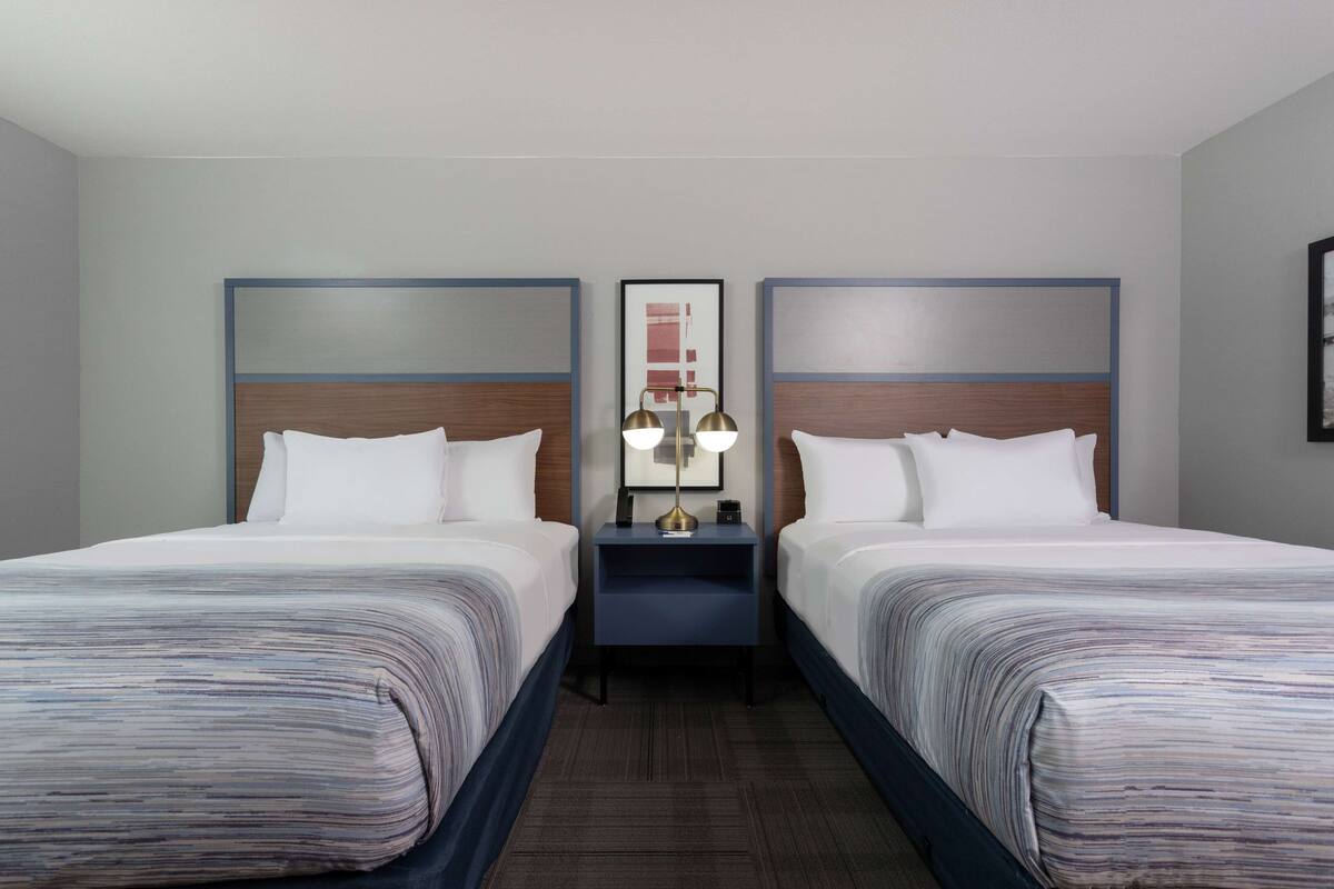 A hotel room with two beds, a nightstand with a lamp, and a framed picture on the wall.