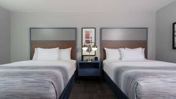 Habitación de hotel con dos camas, una mesita de noche con lámpara y un cuadro enmarcado en la pared.