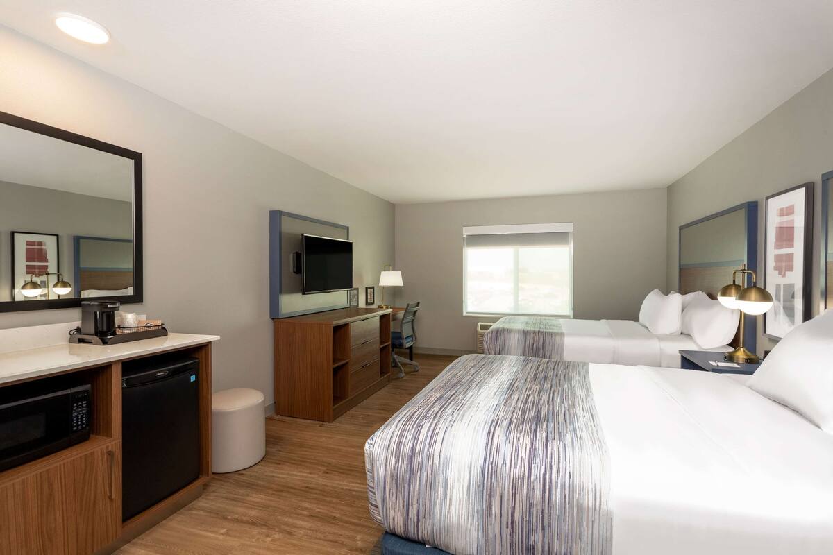 A hotel room with a bed, a desk with a computer, a TV, a coffee maker, and a trash can.