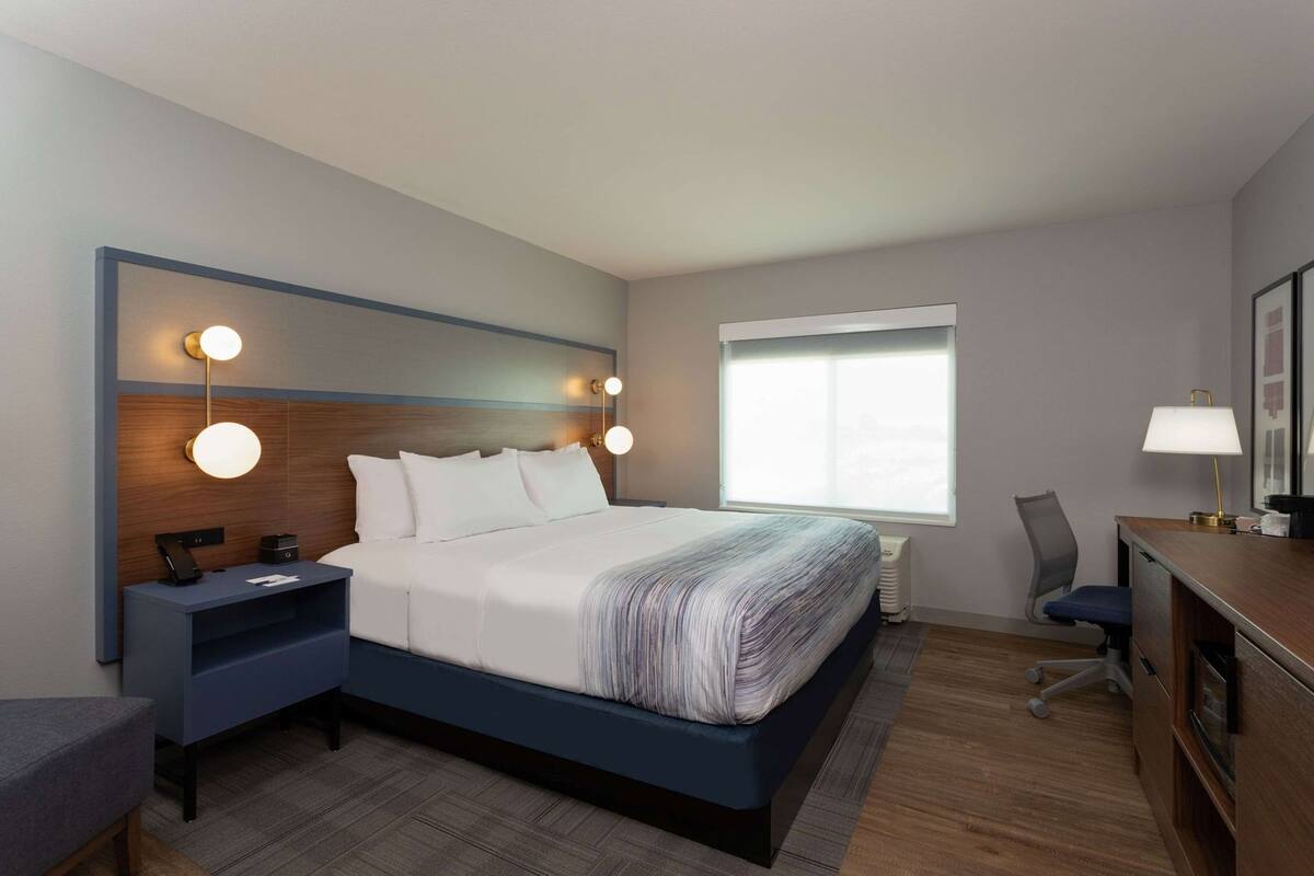 A hotel room with a bed, bedside tables, a desk, a chair, and a window.