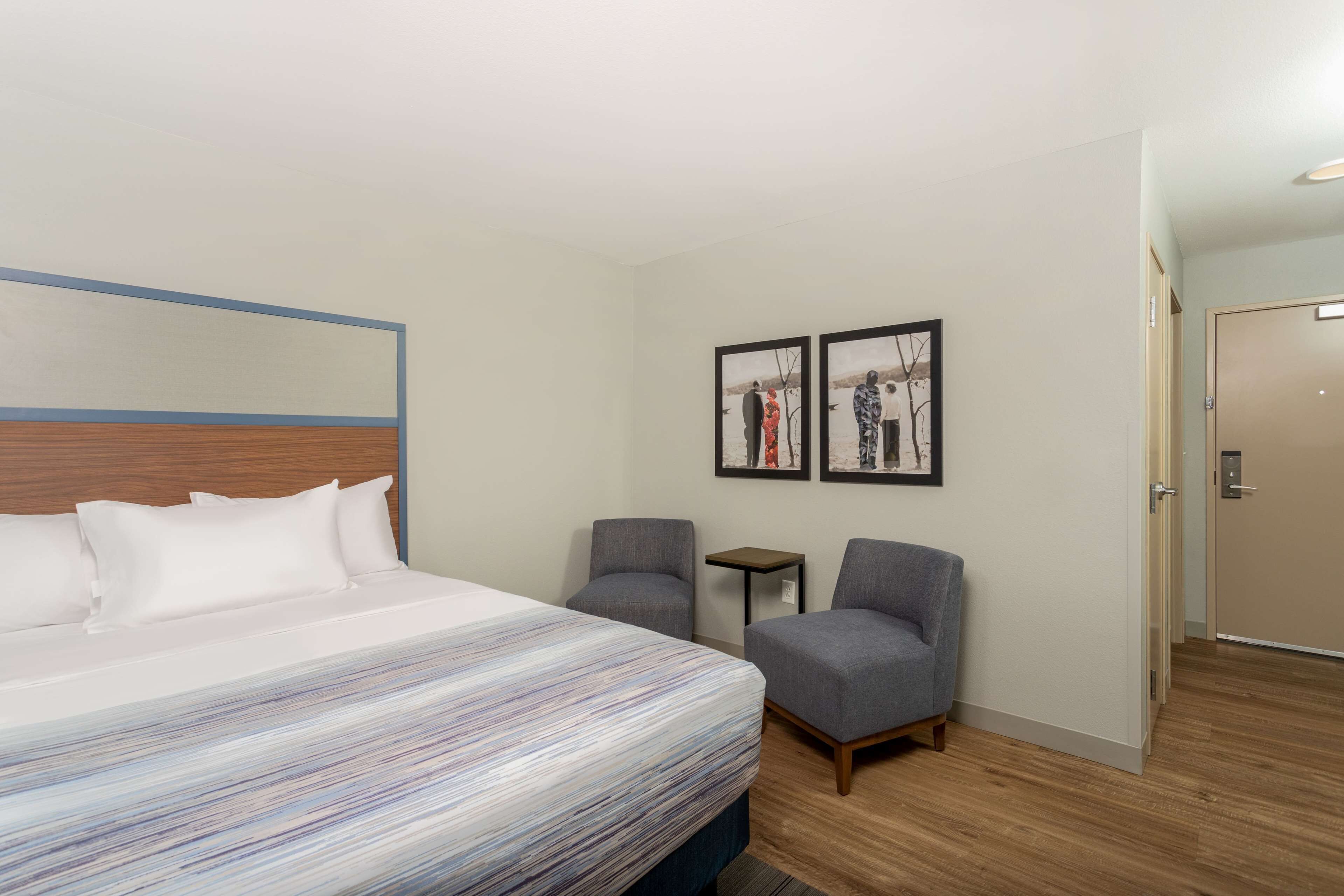 Une chambre d’hôtel avec un lit, deux fauteuils, une petite table et deux tableaux encadrés au mur.