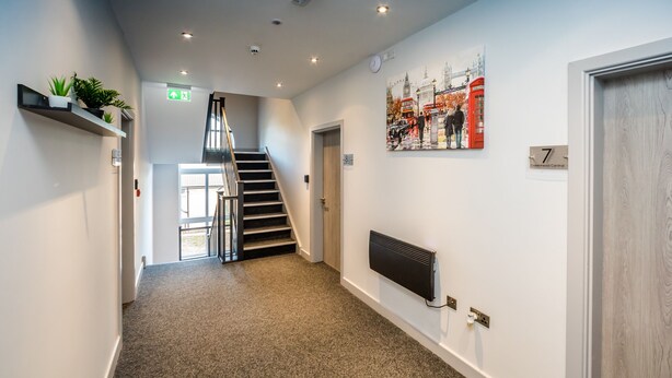 Un couloir doté d’un sol recouvert de moquette, d’un escalier, d’un radiateur, d’un téléviseur fixé au mur et d’une porte portant l’inscription « 7 ».