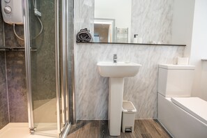 A modern bathroom with a glass shower enclosure, a pedestal sink, and a toilet. - Exquisite Serviced Studio With Private Parking (Huddersfield)