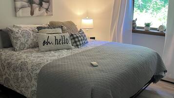 A bedroom with a bed, a ceiling fan, a window with curtains, a bedside lamp, and a painting on the wall.