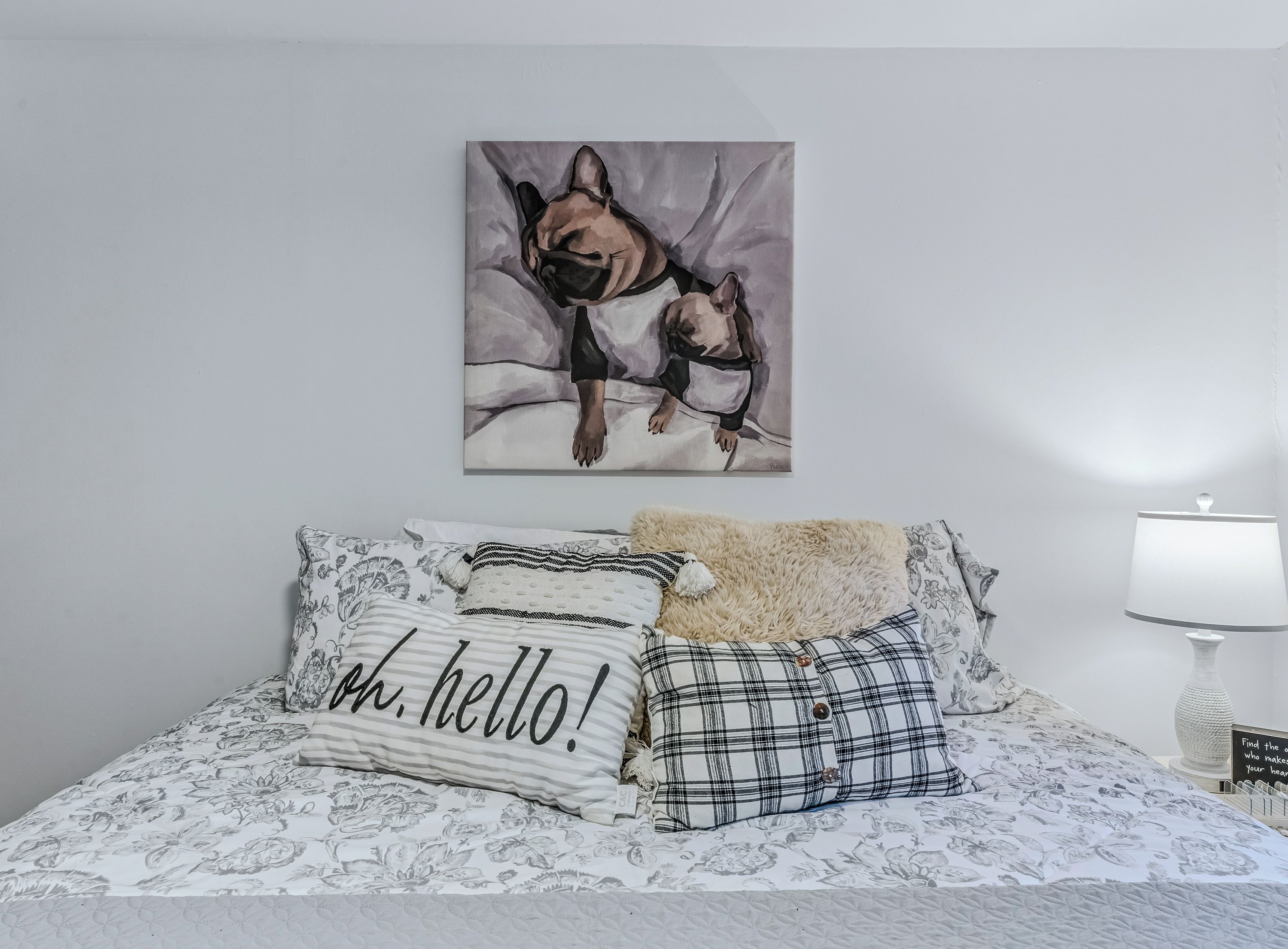 Ein Schlafzimmer mit einem Bett, Kissen, einem Gemälde und einer Nachttischlampe.