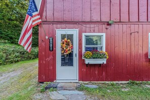 A red wooden building with a white door, a small window, and a flower box with colorful flowers. - Vermont Retreat (Bridgewater)