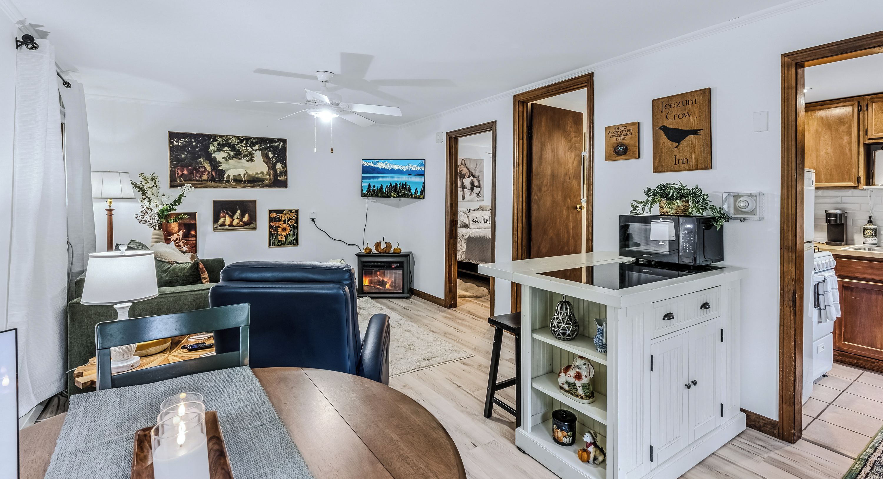 A modern living room with a fireplace, a dining area with a table and chairs, and a kitchen with a microwave and coffee maker.