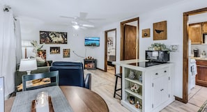 A modern living room with a fireplace, a dining area with a table and chairs, and a kitchen with a microwave and coffee maker. - Vermont Retreat (Bridgewater)