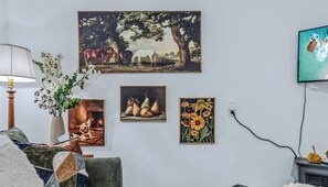 A room with a fireplace, a lamp, and wall-mounted artwork including a painting of horses, a still life of pears, and a painting of sunflowers. - Vermont Retreat (Bridgewater)
