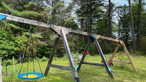 A wooden swing set in a grassy area with trees in the background. - Vermont Retreat (Bridgewater)