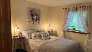 A bedroom with a bed, two bedside tables with lamps, a window with curtains, a wall painting, and a rug. - Vermont Retreat (Bridgewater)