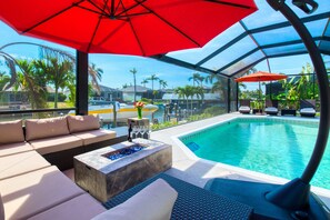 Een zwembadterras met een glazen pool, buitenmeubels en parasols.