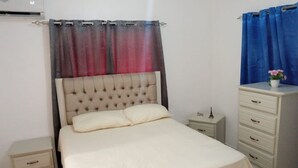 Ein Schlafzimmer mit einem Bett, einem Schminktisch, einem Nachttisch und einem Vorhang.