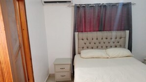 Ein Schlafzimmer mit Bett, Nachttisch, Kommode und Vorhang.