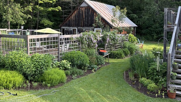 A rustic wooden barn surrounded by lush greenery and a well-maintained garden with various plants and a small pond. - Absolutely Gorgeous Vermont Garden Cottage (Montpelier)