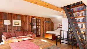 A cozy room with a wooden floor, a sofa, a bed, a bookshelf, and a ladder. - Absolutely Gorgeous Vermont Garden Cottage (Montpelier)