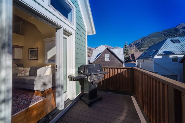 A deck with a grill, a sofa, and a view of a mountain.