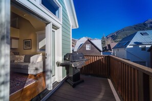 A deck with a grill, a sofa, and a view of a mountain.