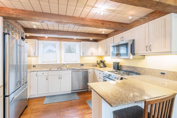 A kitchen with white cabinets, stainless steel appliances, a granite countertop, and wooden beams on the ceiling.