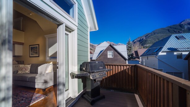 A deck with a grill, a sofa, and a view of neighboring houses and mountains. - Charming Downtown Telluride Retreat | Walk to Main Street, Gondola & Lift 7 (Telluride)