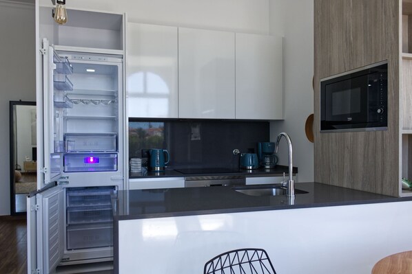Een moderne keuken met witte kastjes, een ingebouwde magnetron en een koelkast met blauwe verlichting.