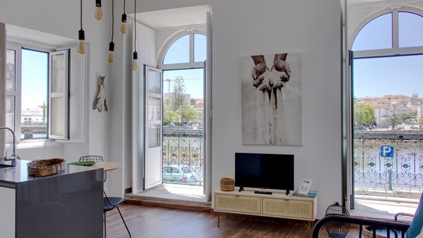 A modern living room with a large TV, open windows, and a balcony with a view of the city. - Apartment with River View, Tavira (Tavira)