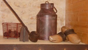 Een rustieke houten plank met een metalen bak, een metalen schep, een metalen zeef en houten klompen.